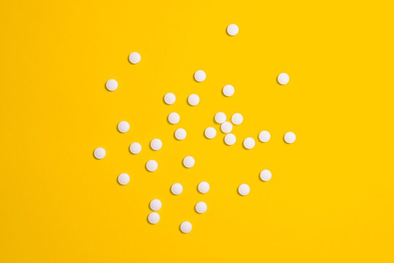 White pills scattered on a vibrant yellow background, symbolizing medical treatment and health care.
