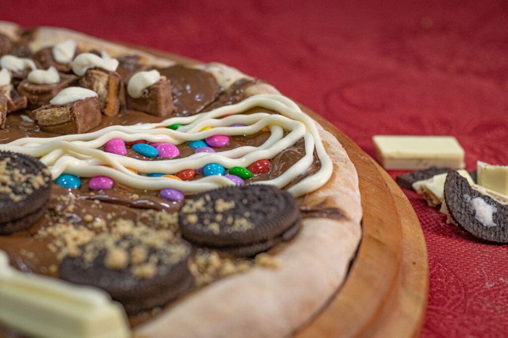 Indulgent dessert pizza topped with chocolate, cream, and colorful candies. Perfect for sweet cravings.