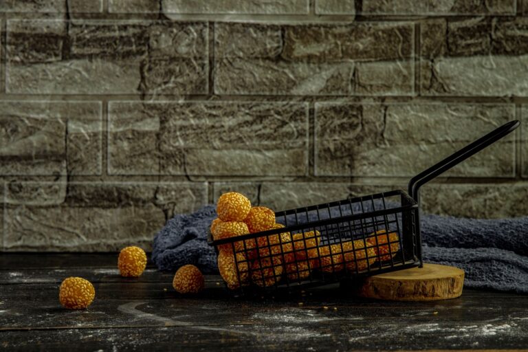 Golden sesame balls in a metal basket against a rustic stone wall background.