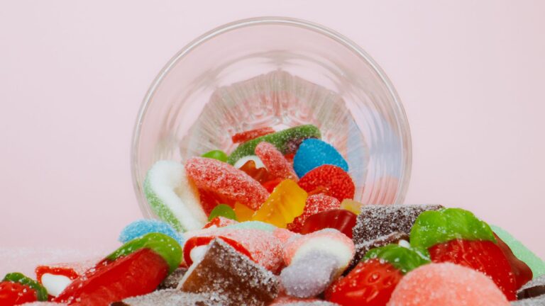 Vibrant sweet gummies spilling from a bowl on a pastel background.