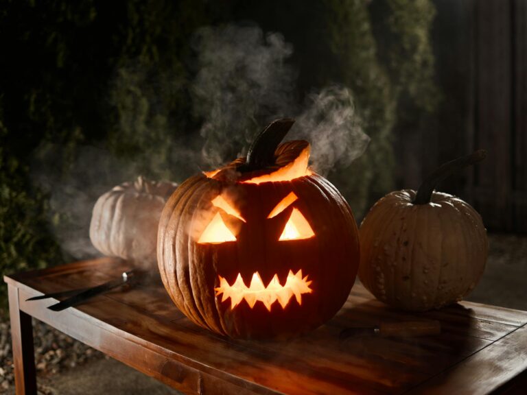 A spooky Jack-o'-lantern emits a warm glow illuminating a wooden table during Halloween night.
