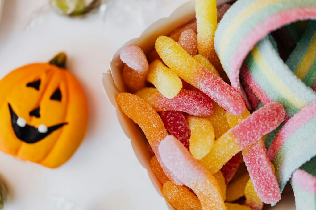 Colorful sour gummy candies and a jack-o'-lantern, perfect for Halloween celebration.