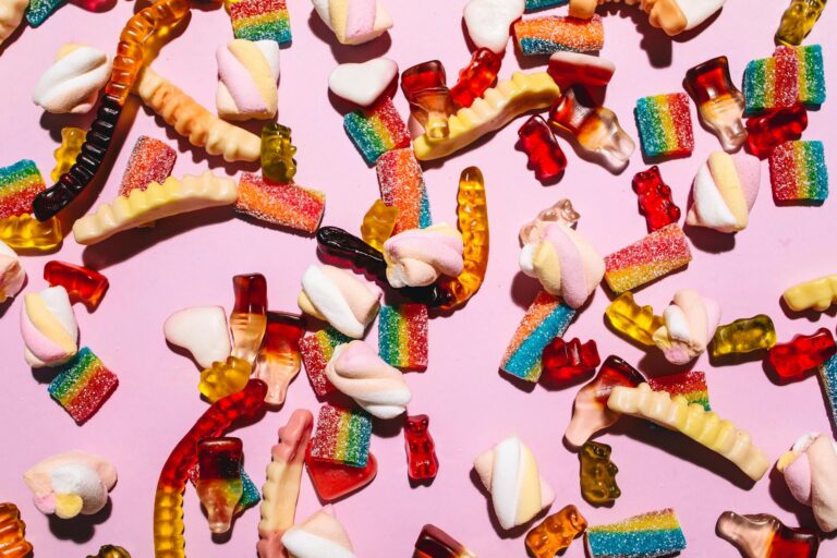 Vibrant array of gummy candies and marshmallows on a pink background, perfect for sweet indulgence.
