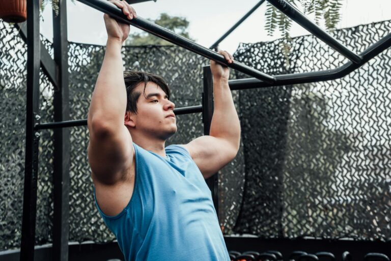 Muscular man in blue tank top performing pull-ups outdoors in Mexico City.