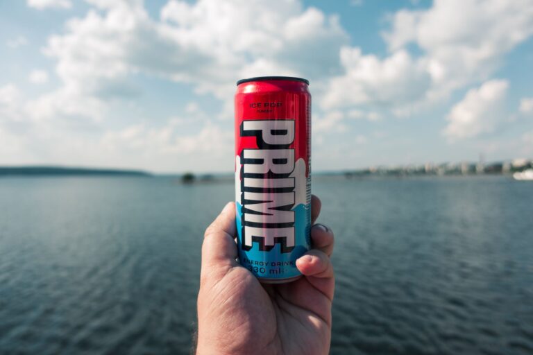 Close-up of a hand holding an energy drink can by a lake on a sunny day in Lahti, Finland.