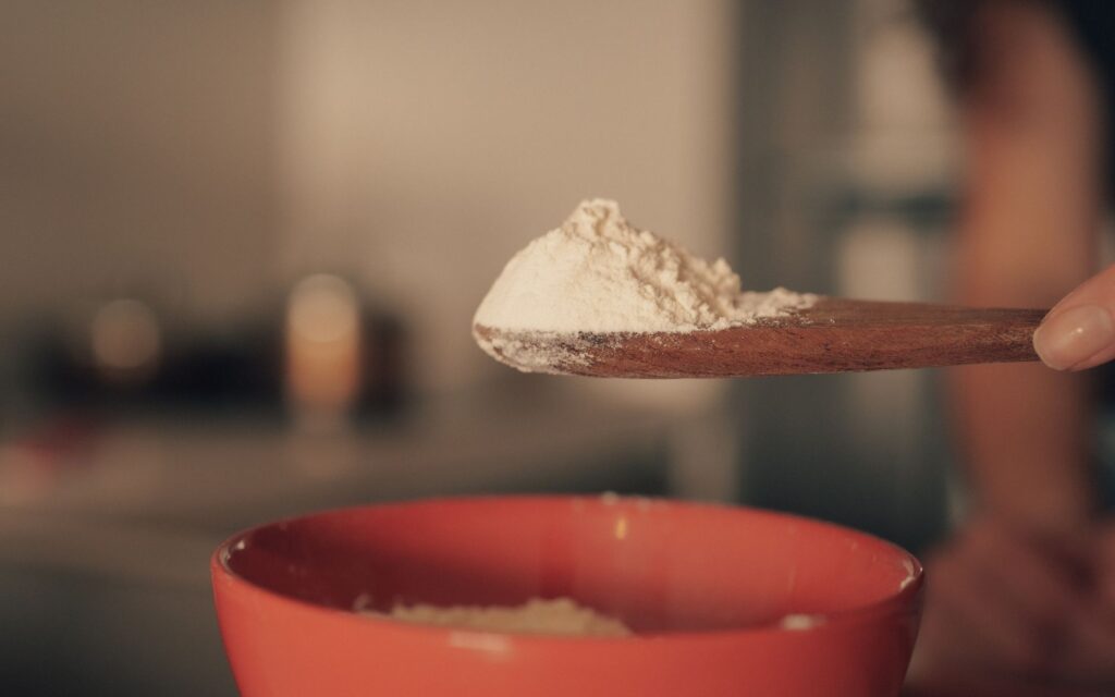 Close-up of flour on a wooden spoon over a red bowl in a kitchen.