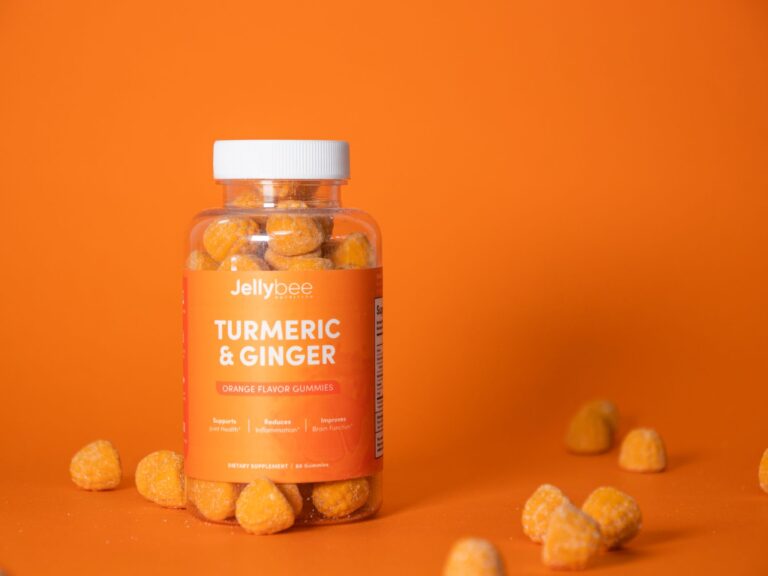 Bright product shot of turmeric and ginger gummies in a plastic bottle against an orange background.