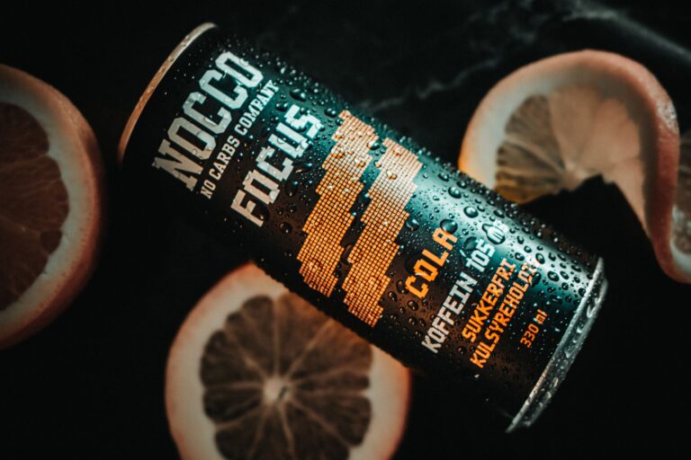 Chilled NOCCO cola energy drink can surrounded by grapefruit slices with water droplets.