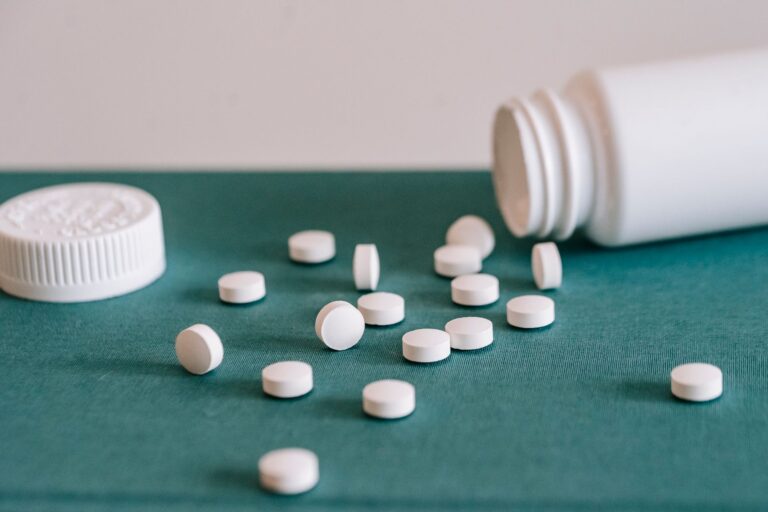 White medical pills spilled out of white plastic jar on green fabric surface against white wall