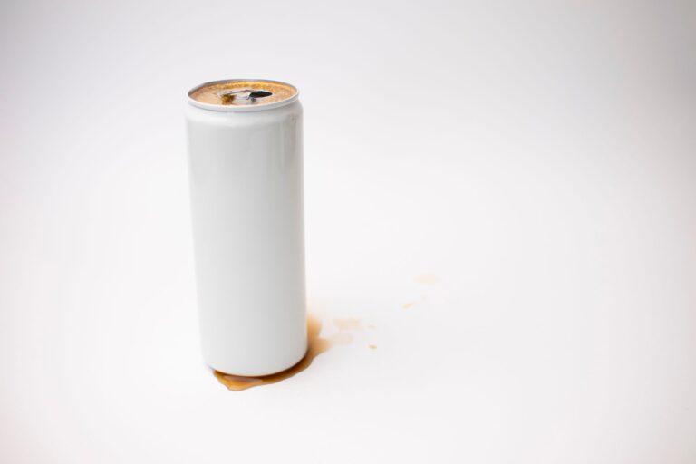 A spilled beverage can with liquid on a minimalist white background.