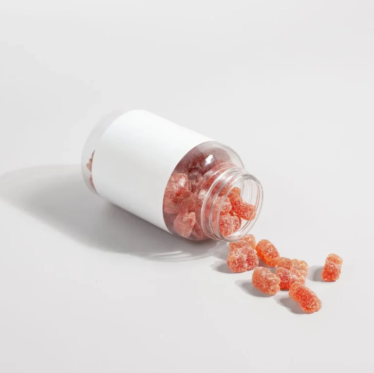 Close-up of gummy vitamins spilled from a clear bottle on a white surface