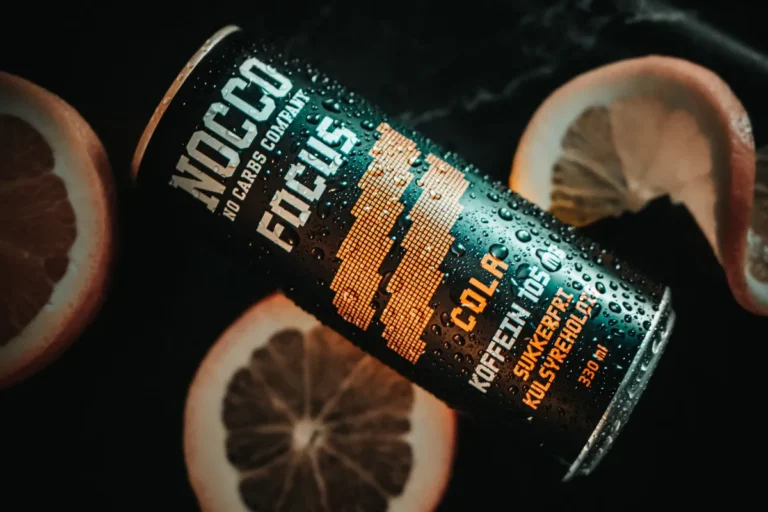 Chilled NOCCO cola energy drink can surrounded by grapefruit slices with water droplets.